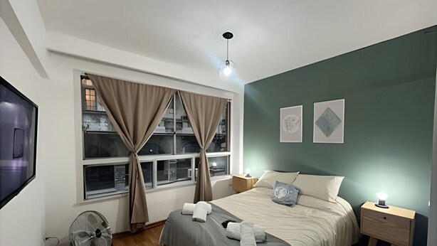 A bedroom with a bed, bedside tables, a fan, a window with curtains, and artwork on the wall. - Home in downtown-Maipu St. (Buenos Aires)