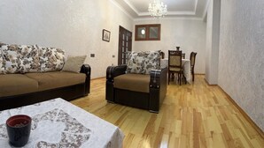A living room with a sofa, armchair, dining table, and chandelier. - Nermanov Home (Baku)