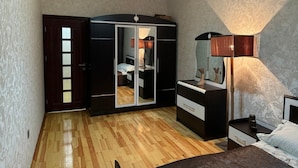 A bedroom with a wooden floor, a wardrobe with a mirror, a bedside table, and a lamp. - Nermanov Home (Baku)