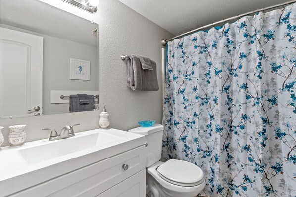 Un baño con un lavamanos blanco, inodoro y cortina de ducha estampada con motivos florales.