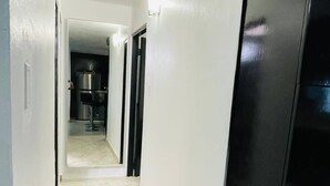 Un pasillo con suelo de baldosas, paredes blancas y una puerta negra a la derecha.