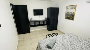 Un dormitorio con cama, escritorio con silla, televisión y armario.