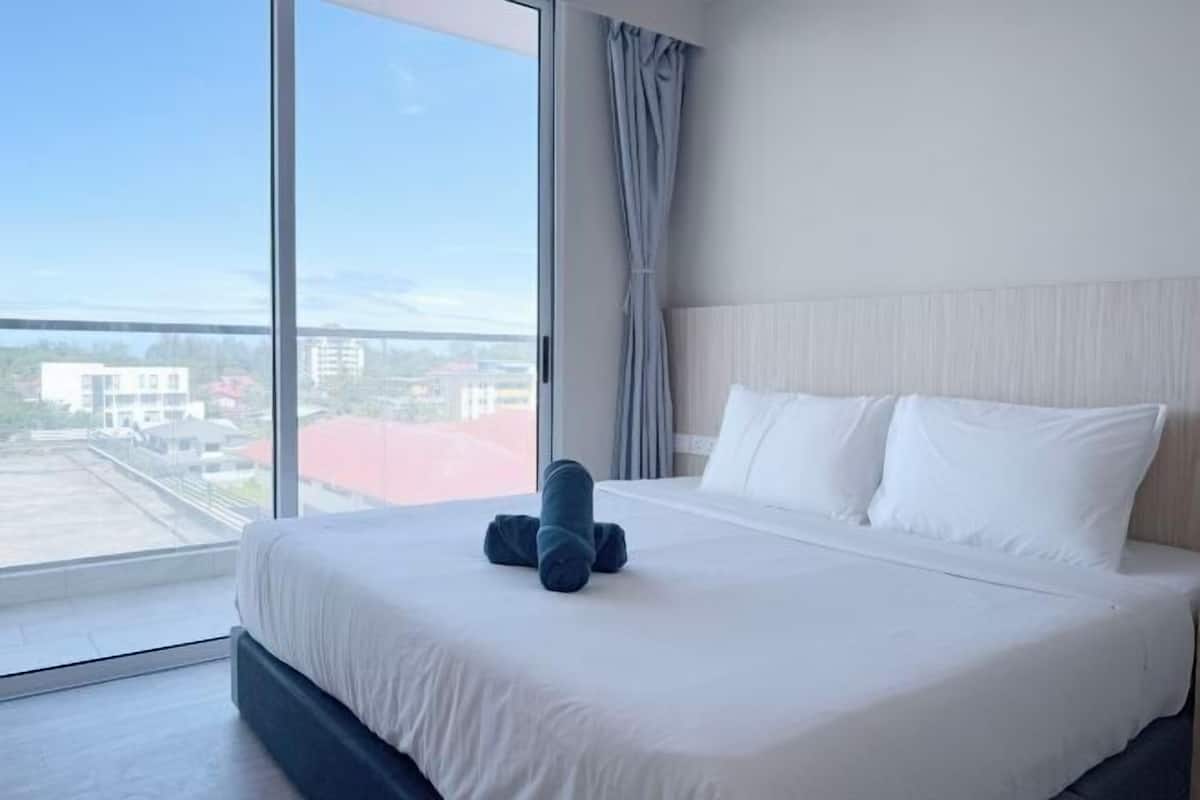 Une chambre d’hôtel avec une grande fenêtre, un lit avec du linge de lit blanc et une vue sur les bâtiments environnants.