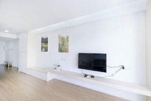 A modern living room with a flat-screen TV mounted on the wall, a white bench, and two framed pictures.