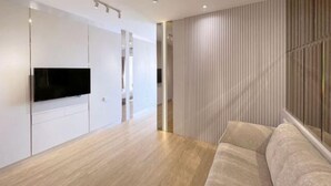 A modern living room with a flat-screen TV mounted on a white cabinet, a beige sofa, and a wooden floor.