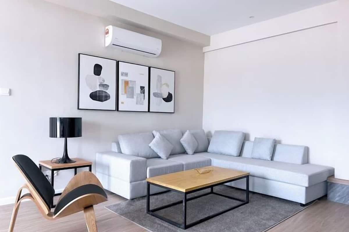 Un salon moderne avec un canapé gris, une table basse en bois, un lampadaire noir et des œuvres d’art encadrées accrochées au mur.