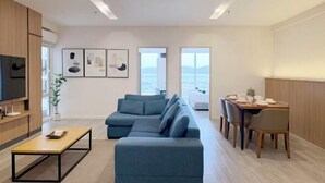 A modern living room with a sectional sofa, a dining table with chairs, a TV, and artwork on the wall.