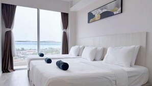 A hotel room with a large window, a bed with white bedding, and a painting on the wall.