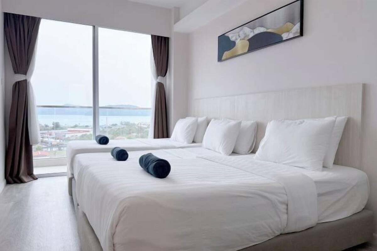 Une chambre d’hôtel avec une grande fenêtre, un lit recouvert de draps blancs et un tableau accroché au mur.