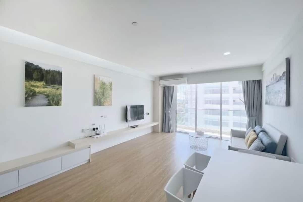 Un salon moderne et minimaliste, doté d’une grande fenêtre, d’un canapé, d’un téléviseur et d’œuvres d’art accrochées aux murs.