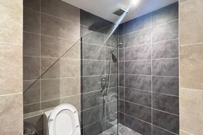 A modern bathroom with a glass-enclosed shower, a toilet, and tiled walls.