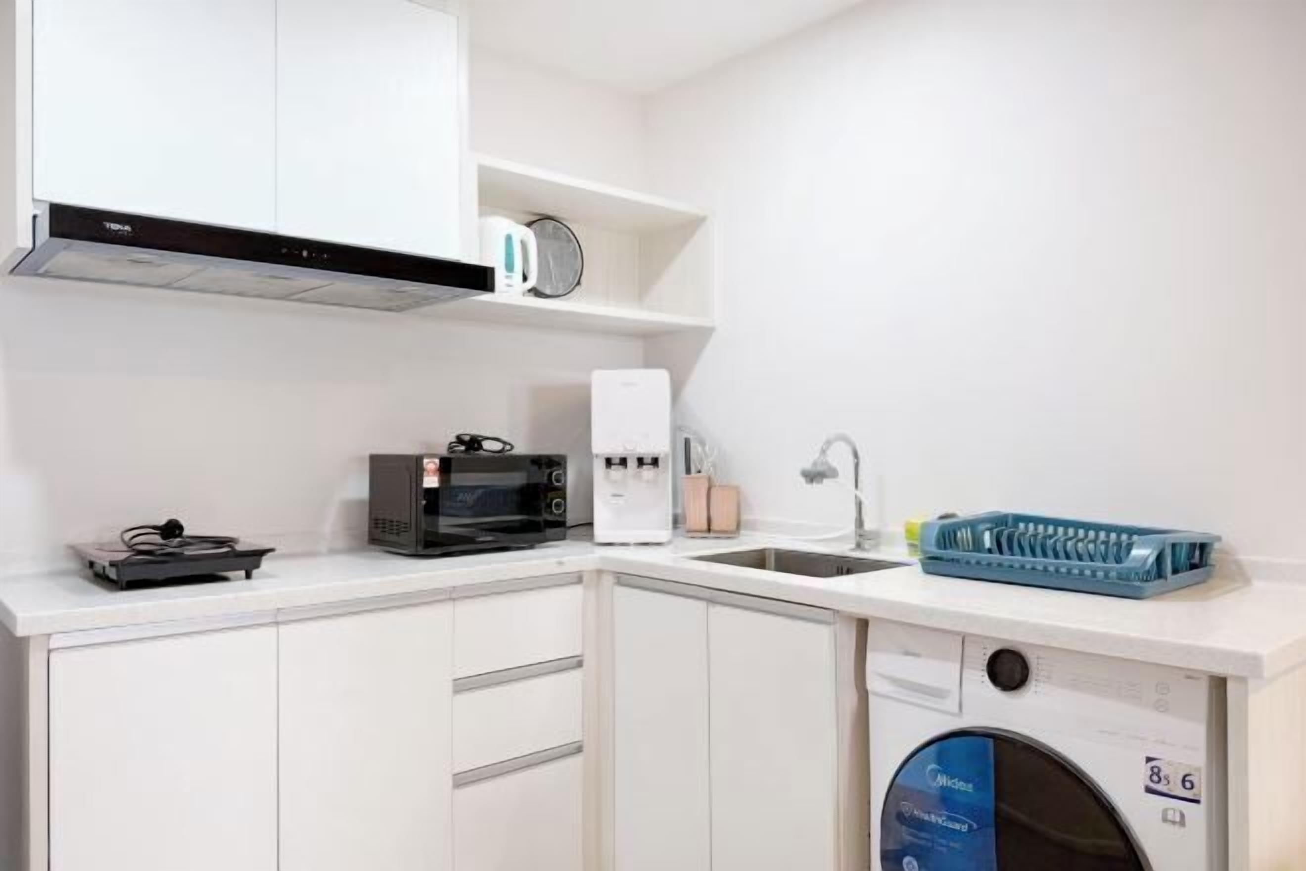 Una cocina compacta con armarios blancos, microondas, cafetera y lavavajillas.