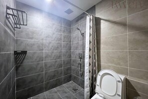 A modern bathroom with grey tiles, a shower, a toilet, and a towel rack.