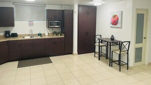 A compact kitchen with dark cabinets, a microwave, and a sink. There is a dining area with a table and chairs. - Carolina Green House (Carolina)