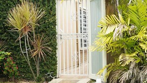 A pathway leading to a gated entrance with a lush green hedge and palm trees. - Carolina Green House (Carolina)