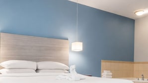 Une chambre d’hôtel moderne avec un grand lit, une tête de lit, une lampe suspendue et une salle de bain équipée d’une baignoire et d’un lavabo.