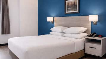 Habitación de hotel con cama, mesitas de noche, un velador con teléfono y un cuadro colgado en la pared.