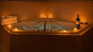 Une baignoire remplie de pétales de roses, avec des bougies et des verres à vin.
