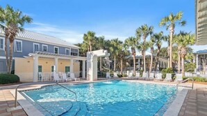 A swimming pool with lounge chairs, palm trees, and a building with a light-colored facade. - Coastal Breeze - Private Beach & Pool + Free Golf Cart (Miramar Beach)