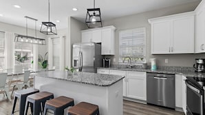 A modern kitchen with white cabinets, a granite countertop, stainless steel appliances, and bar stools. - Coastal Breeze - Private Beach & Pool + Free Golf Cart (Miramar Beach)