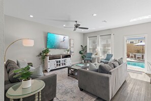 A modern living room with a grey sofa, a glass coffee table, and a flat-screen TV mounted on the wall.