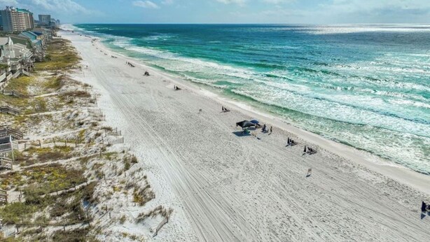 A beach with a long stretch of sand, a few umbrellas, and a few people. There are buildings along the beach. - Coastal Breeze - Private Beach & Pool + Free Golf Cart (Miramar Beach)
