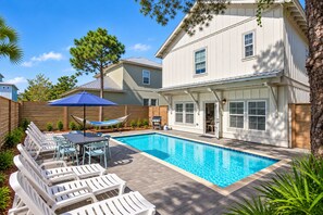 A backyard with a swimming pool, lounge chairs, a barbecue grill, and a wooden fence.