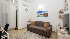 A living room with a brown sofa, a painting of a cityscape, a clock, and a television. - 1 bedroom nice home in Siracusa (Siracusa)