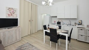 A modern, well-lit living room with a flat-screen TV, a dining area with a table and chairs, and a kitchen with white cabinets and appliances. - 1 bedroom nice home in Siracusa (Siracusa)