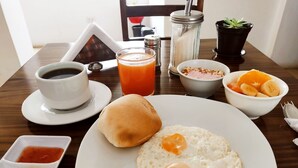 Ein Frühstückstisch mit Spiegeleiern, einer Kaffeetasse, einem Glas Orangensaft, einer Obstschale und einer kleinen Portion Ketchup.