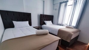 Ein Hotelzimmer mit zwei Betten, jeweils mit Kopfteil, Nachttisch und einem Vorhangfenster.