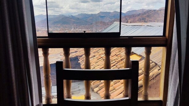 Ein Zimmer mit Blick auf Stadt und Berge, durch ein Fenster. Im Vordergrund steht ein hölzerner Stuhl.