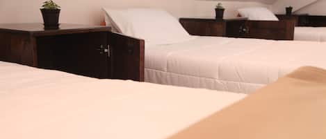 A hotel room with three beds arranged in a row, each with a wooden nightstand and a potted plant.