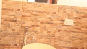 Ein Badezimmer mit Wand aus Steinplatten, einem weißen Waschbecken, einem Handtuch und einem Spiegel, der eine Tür reflektiert.
