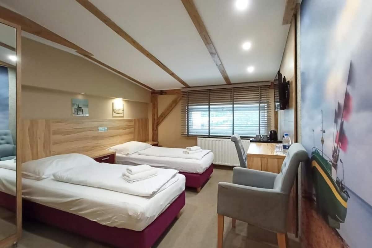 Une chambre avec deux lits, un bureau, une chaise et une fenêtre avec des stores.