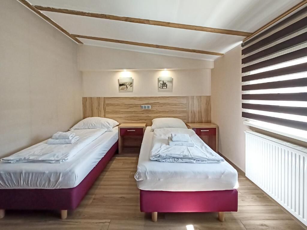 A room with two beds, wooden headboard, bedside tables, and wall-mounted lights.