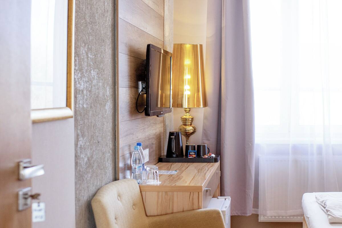 Une chambre d’hôtel avec un plancher en bois, un fauteuil beige, un petit bureau avec une lampe, une télévision et un lit.
