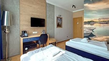 A hotel room with a desk, a flat-screen TV, a bed with two pillows, and a mural of a harbor scene.