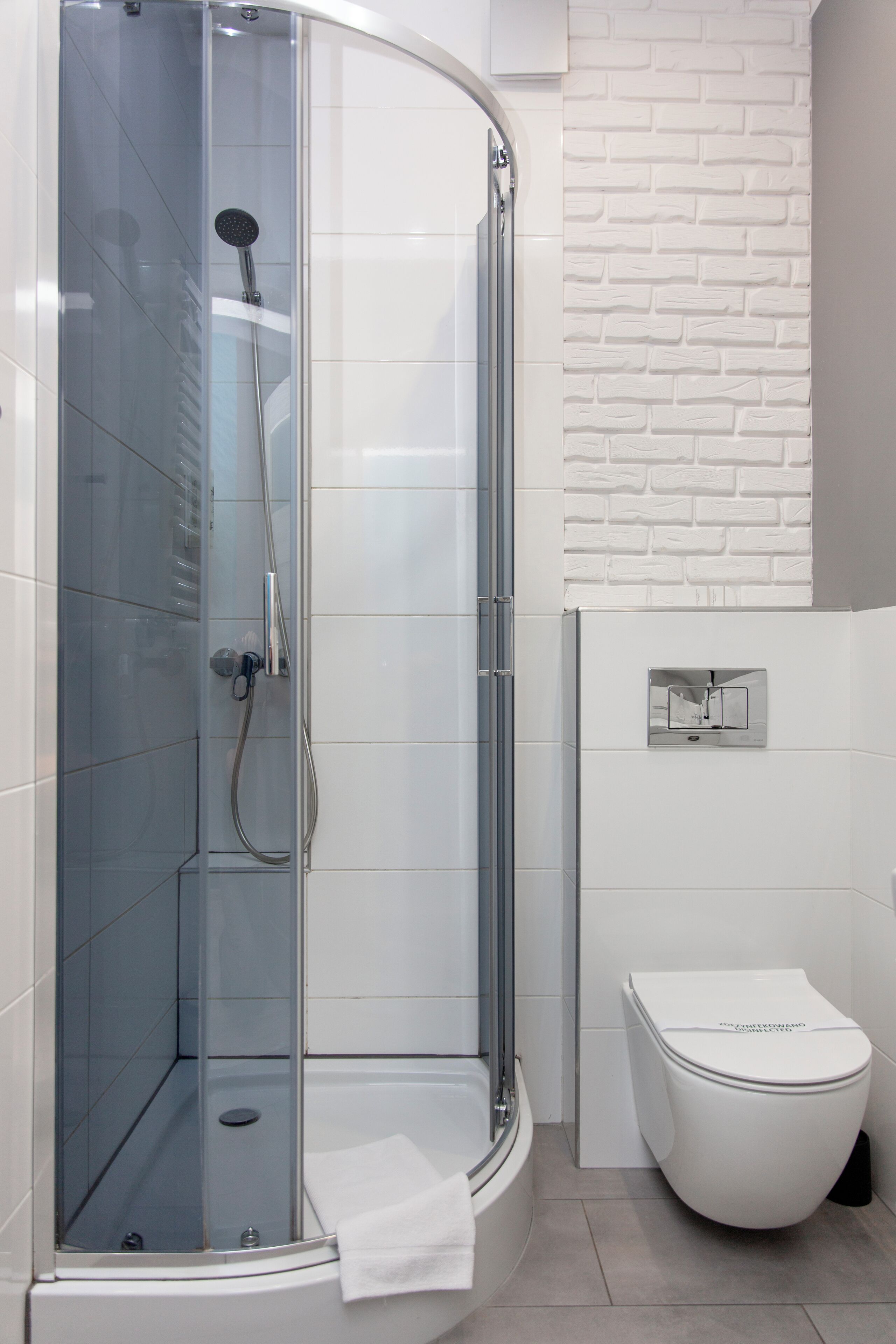 A modern bathroom with a glass-enclosed shower, a white toilet, and a tiled wall with a brick pattern.