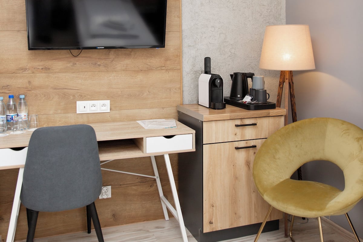 Une chambre d’hôtel moderne équipée d’un bureau en bois, d’un téléviseur à écran plat, d’une lampe, d’une chaise et d’une machine à café.