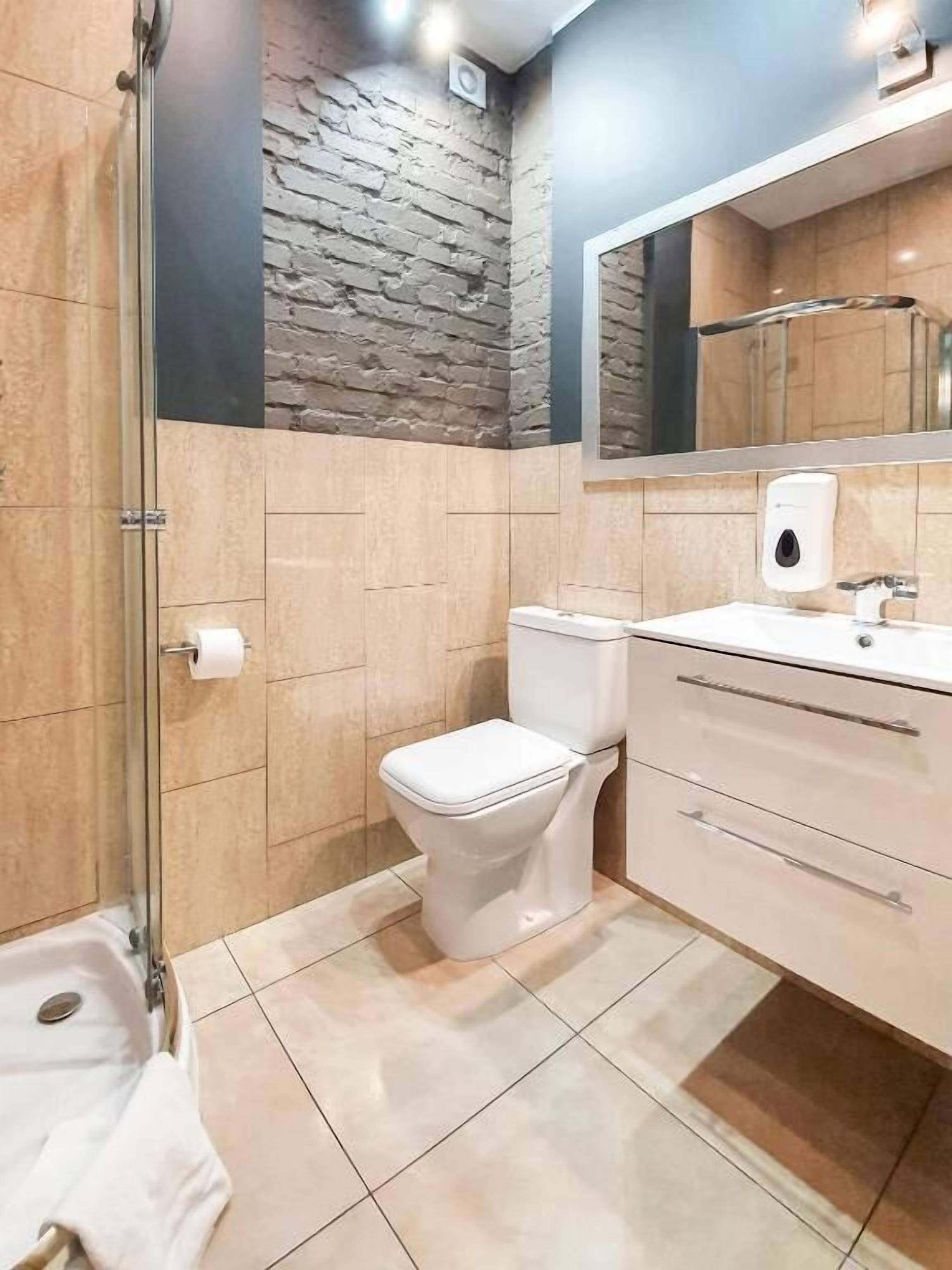 A bathroom with a toilet, a sink, a mirror, and a glass shower enclosure.