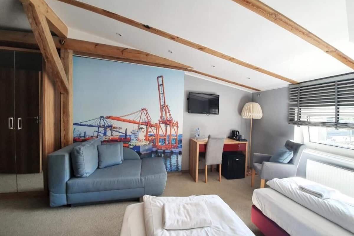 Une chambre d’hôtel avec un grand lit, un canapé, un bureau avec une chaise, une télévision et une fenêtre avec des stores.