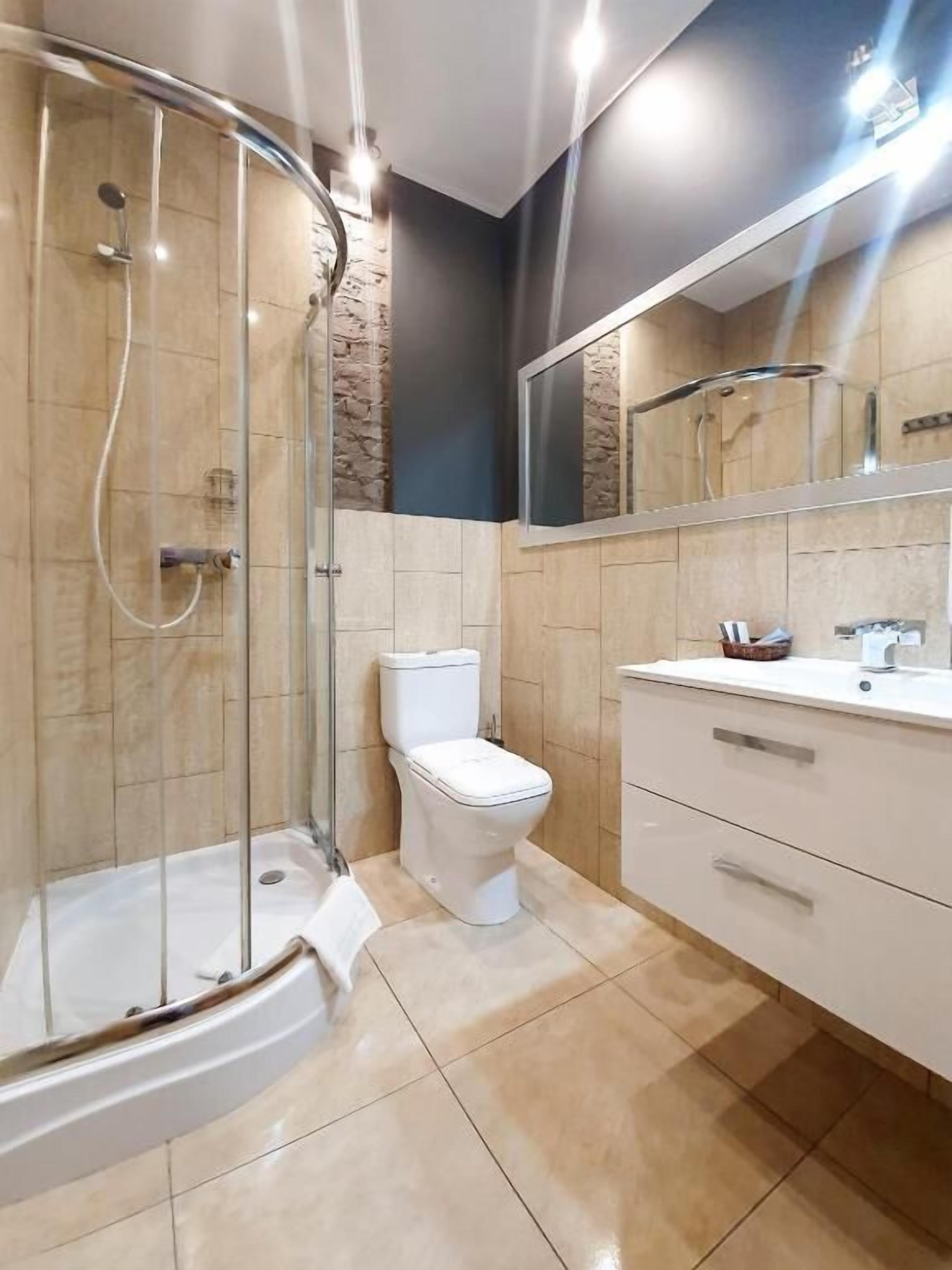 A modern bathroom with a glass-enclosed shower, a toilet, and a vanity with a mirror.
