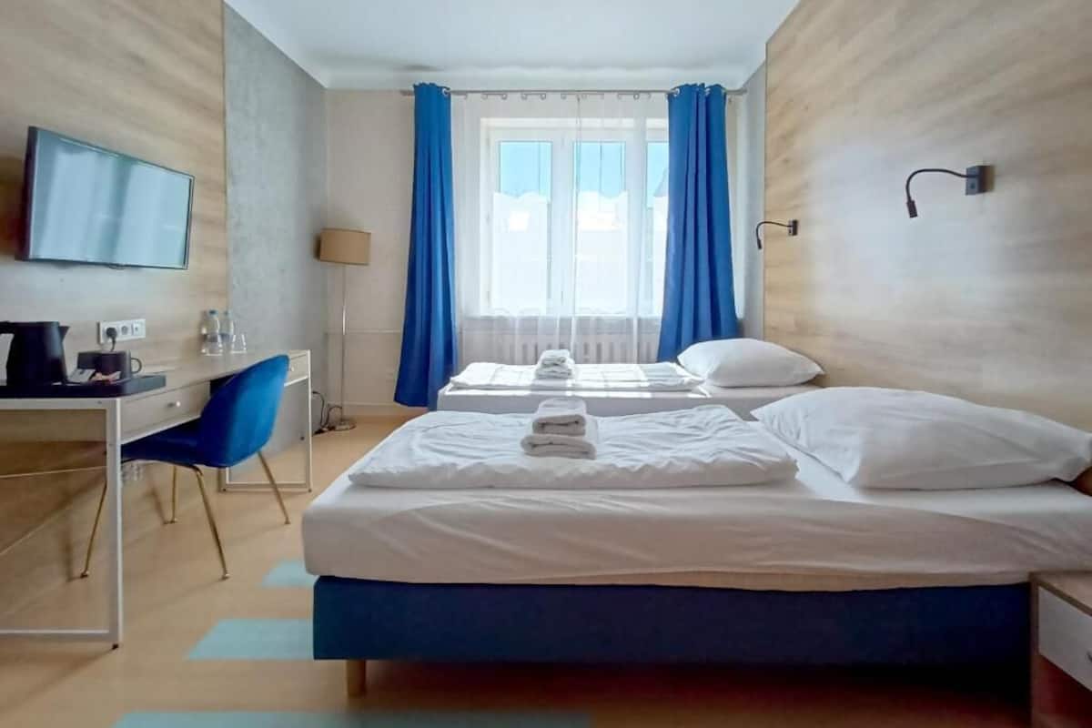 Une chambre d’hôtel équipée d’un lit, d’un bureau, d’une chaise, d’une télévision et d’une fenêtre avec des rideaux.