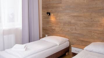 Ein Hotelzimmer mit zwei Betten, Holzboden, einem Fenster mit durchscheinenden Vorhängen und einer Wandleuchte.