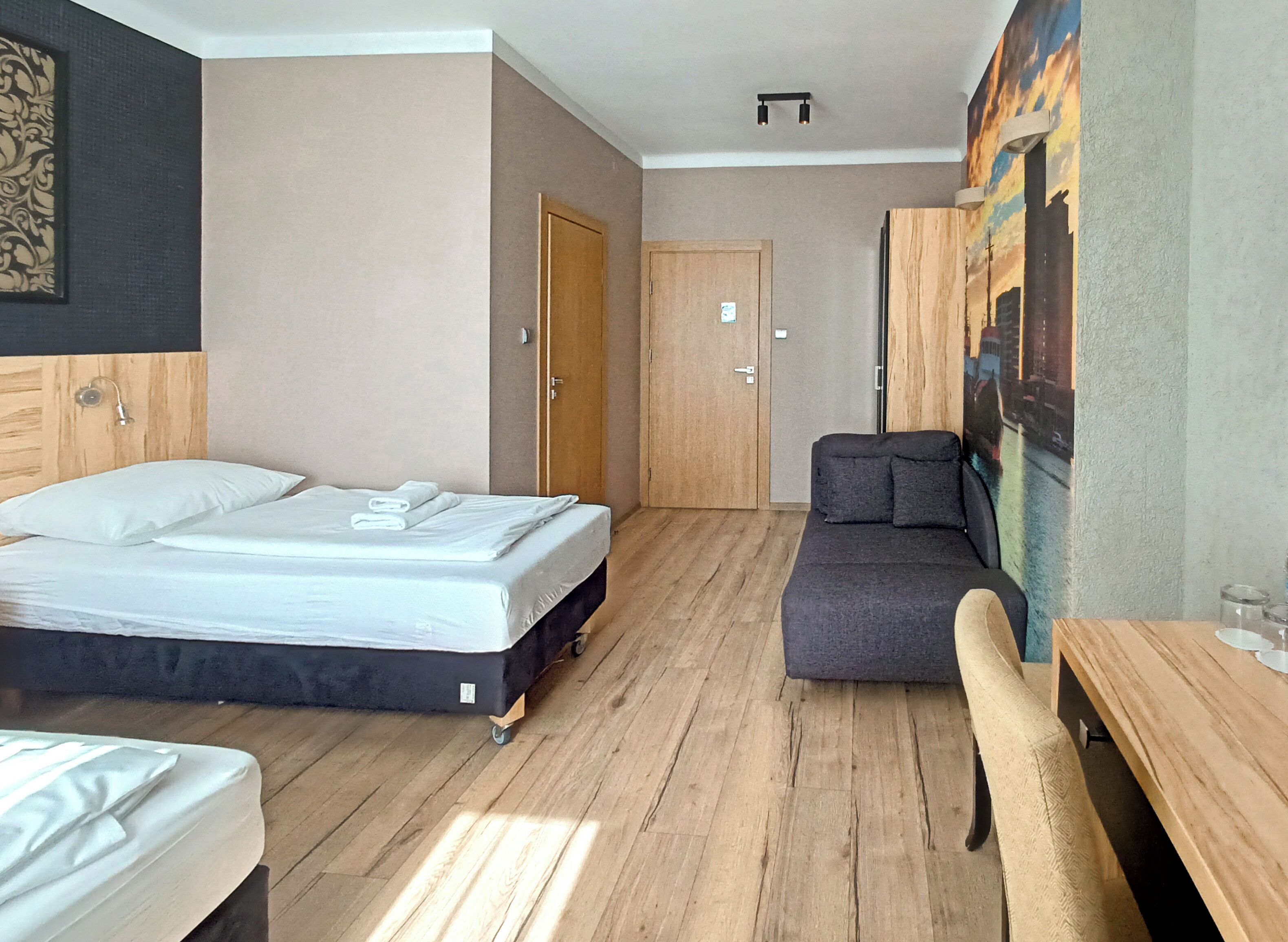 A hotel room with a bed, a sofa, a wooden table, and a door.