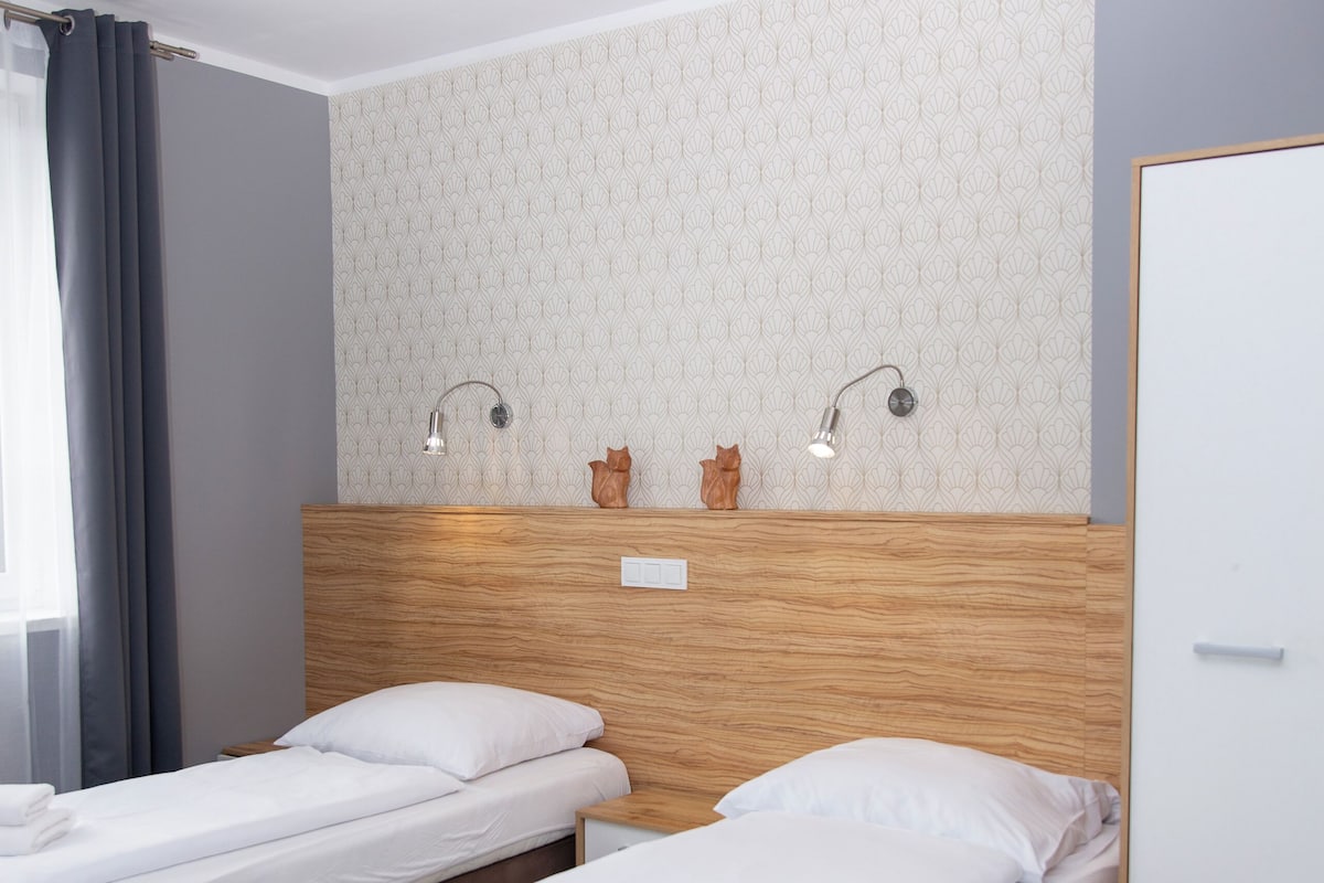 Une chambre d’hôtel avec deux lits simples, une tête de lit en bois, une table de chevet, une petite table et une lampe de chevet.