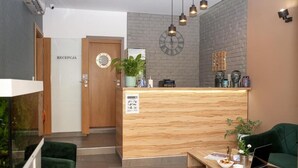Un espace d’accueil avec un comptoir de réception en bois, une horloge au mur et un canapé vert.