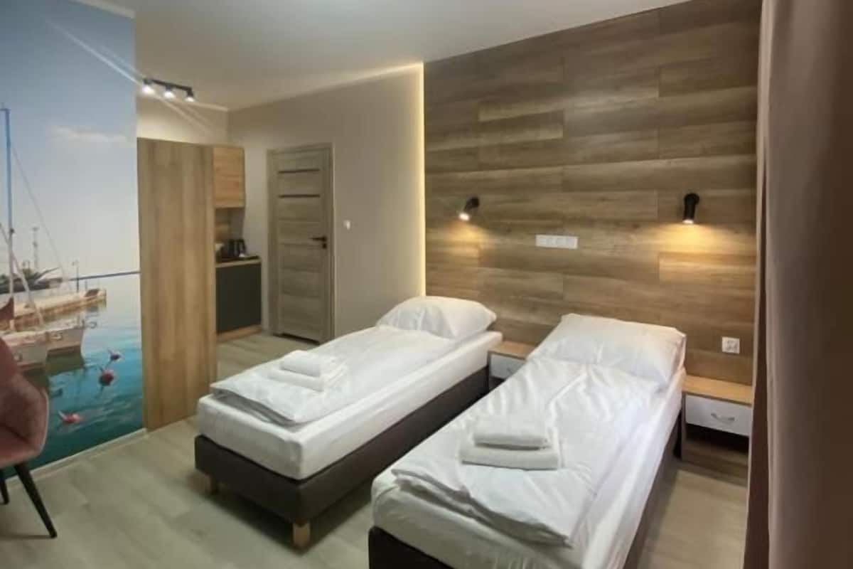 Une chambre d’hôtel avec deux lits simples, un mur décoratif en bois, une fresque représentant un port et une petite kitchenette.