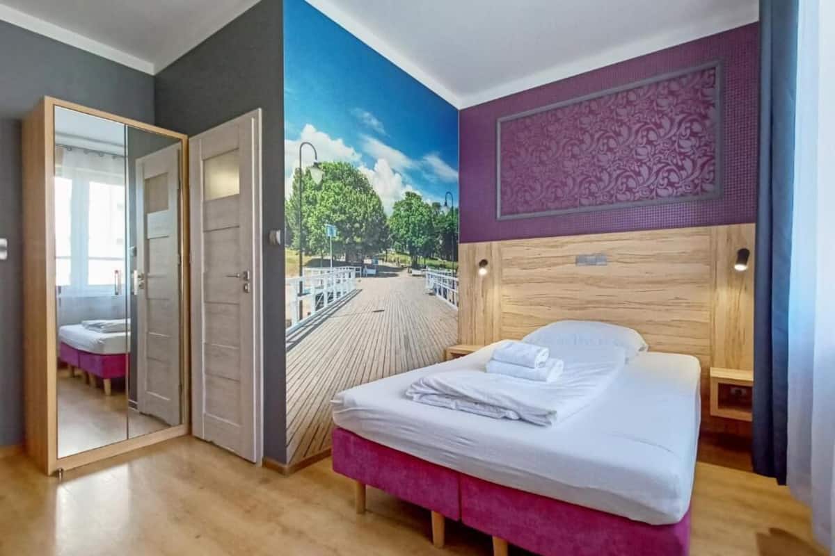 Une chambre à coucher avec un lit, un miroir, une fresque murale et une tête de lit en bois.